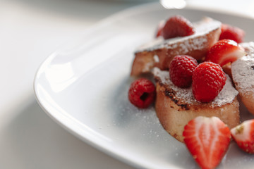 French toast with strawberries and raspberries, sprinkled with powdered sugar. Dessert on a white plate.