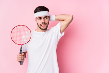 Young caucasian man playing badminton isolated touching back of head, thinking and making a choice.