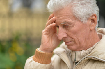 Serious senior man thinking in park on green background