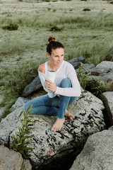 Naklejka na ściany i meble Young Woman Sitting On A Rock Holding A Cup, Relaxed Yoga Lifestyle Concept