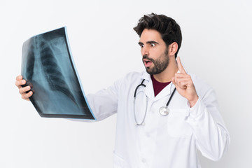 Young handsome man with beard over isolated white background wearing a doctor gown and holding a bone scan