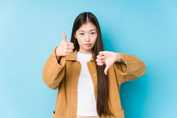 Young chinese woman posing in a blue background isolated showing thumbs up and thumbs down, difficult choose concept