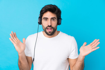 Young handsome man with beard over isolated blue background surpeised and listening music