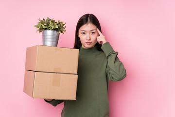 Young chinese woman holding boxes isolated pointing temple with finger, thinking, focused on a task.