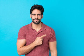 Young handsome man with beard over isolated blue background pointing to the side to present a...