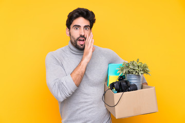 Young handsome man with beard making a move while picking up a box full of things over isolated...