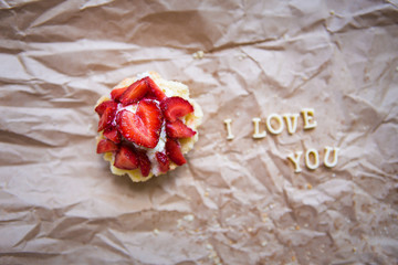 Bright cupcake with strawberries lies on craft paper, the inscription I love you