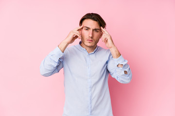 Young caucasian man posing in a pink background isolated focused on a task, keeping forefingers pointing head.