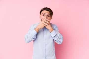Young caucasian man posing in a pink background isolated shocked covering mouth with hands.