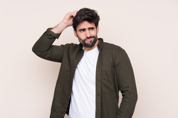 Young handsome man with beard over isolated background having doubts while scratching head