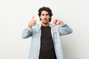 Young handsome man against a white background showing thumbs up and thumbs down, difficult choose concept