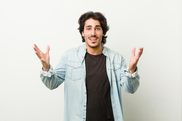 Young handsome man against a white background receiving a pleasant surprise, excited and raising hands.