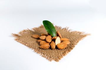 Close up of healthy raw almonds placed on a rustic woven brown mat, decorated with green leaves,...