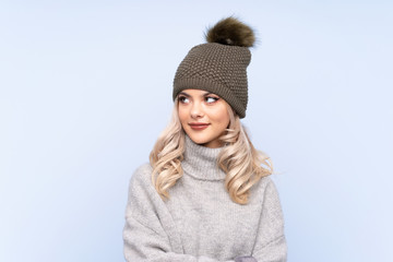 Young teenager girl with winter hat over isolated blue background standing and looking to the side
