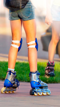 Beautiful long-legged girl posing on a vintage roller skates in denim shorts and white T-shirt in the skate park on a warm summer evening. Part of body. .