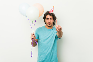 Young man celebrating a party holding balloons showing number one with finger.
