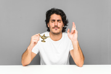 Young man holding a magic lamp crossing fingers for having luck