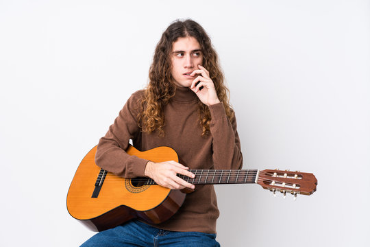 Young caucasian man playing guitar isolated relaxed thinking about something looking at a copy space.