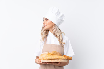 Teenager girl in chef uniform. Female baker holding a table with several breads over isolated white background looking to the side