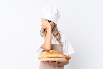 Teenager girl in chef uniform. Female baker holding a table with several breads over isolated white background covering eyes and looking through fingers