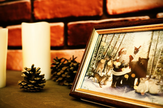 Chrismas Santa Claus picture with animals standing on fireplace among pine cones and white candles