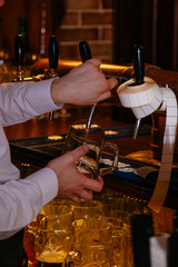 Bartender pouring draft beer from the crane into the glass in pub