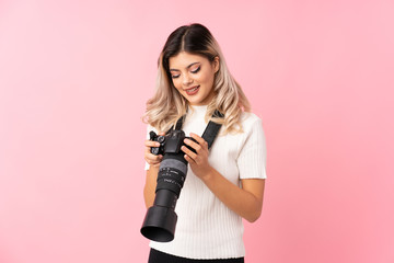 Teenager girl over isolated pink background with a professional camera