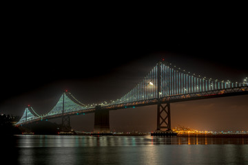 Night View of the Lit Up Oakland Bridge With Clear Skies and Moon in the Horizon