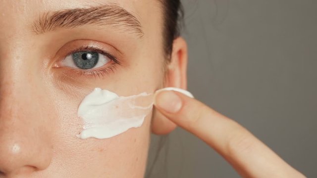 Young woman puts a white cream on her face