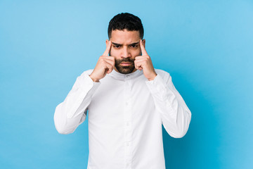 Young latin man against a blue  background isolated focused on a task, keeping forefingers pointing head.