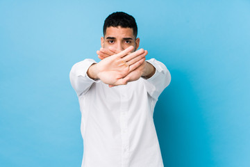 Young latin man against a blue  background isolated doing a denial gesture
