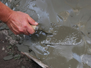 a man's hand works with a spatula leveling the cement layer