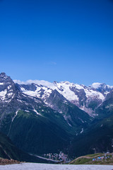 Vertical beautiful panorama of the Caucasus mountains. The top of the mountain range covered with snow. Forest on the slope. Sunny day. Background image for travel and nature.