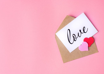 Valentines Day concept. Greeting card with the inscription love in an open envelope, two pink and red hearts on a pink background. Top view, copy space