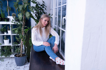 blonde girl sits by the window and thinks about something