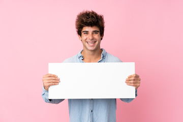Young caucasian man over isolated pink background holding an empty white placard for insert a...