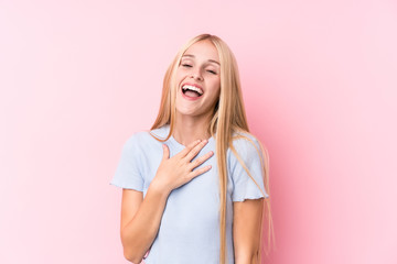 Young blonde woman on pink background laughs out loudly keeping hand on chest.