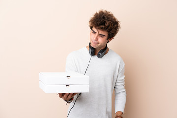 Young handsome man holding a pizza over isolated wall with sad expression