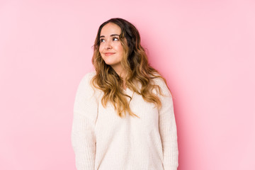 Young curvy woman posing in a pink background isolated dreaming of achieving goals and purposes
