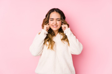 Young curvy woman posing in a pink background isolated covering ears with hands.