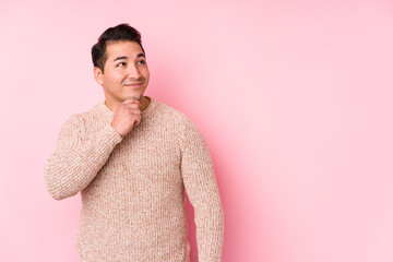 Young curvy man posing in a pink background isolated looking sideways with doubtful and skeptical expression.