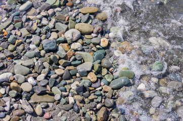 pebble coastline. Seashore with transparent water and small stones.