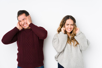 Young couple posing in a white background covering ears with hands.