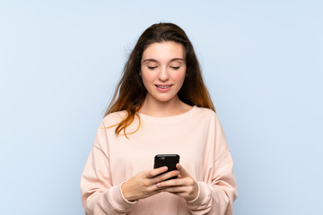 Young brunette girl over isolated blue background sending a message or email with the mobile