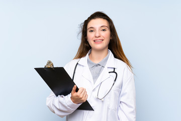 Young brunette girl over isolated blue background with doctor gown and holding a folder