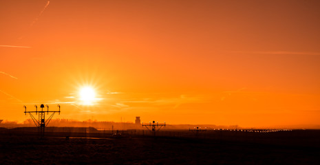 Silhouette of airport at sunny orange and purple sunset. Runway end identification lights and bright sun.