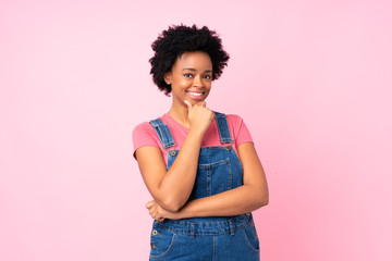 African american woman with overalls over isolated pink background laughing