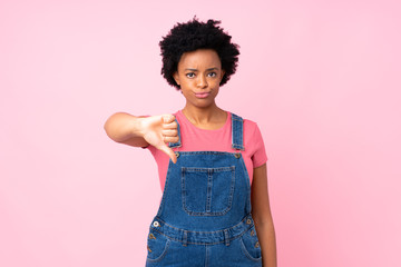 African american woman with overalls over isolated pink background showing thumb down sign