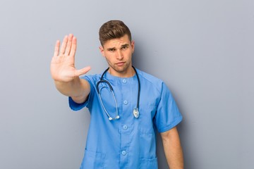 Young nurse man standing with outstretched hand showing stop sign, preventing you.