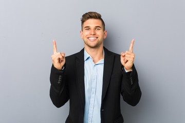 Young handsome caucasian man indicates with both fore fingers up showing a blank space.